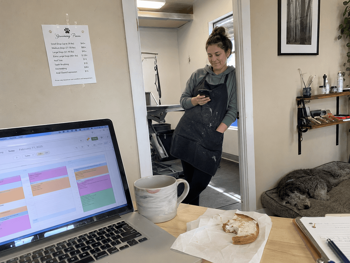Owner of The Sudsy Puppy checking her phone next to a laptop showing the Groomify calendar